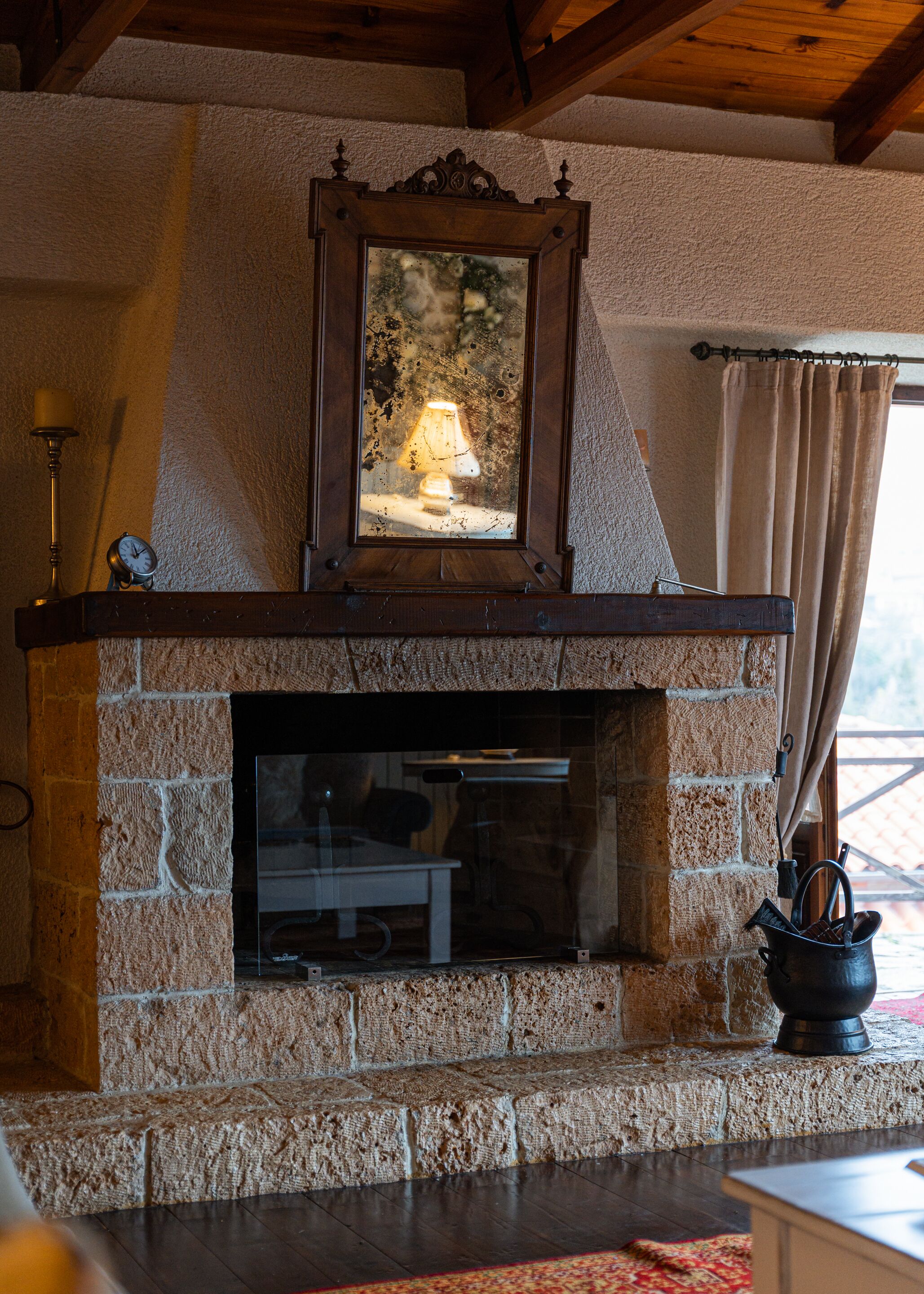 A stone fireplace with a wooden mantel, a mirror above it, and a small table with a lamp.