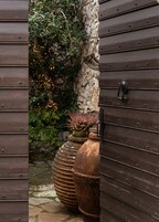 Una puerta de madera con un picaporte metálico, un muro de piedra y una maceta con follaje rojo.