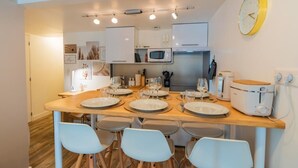 Een moderne keuken met een houten eettafel voor vier personen, witte kastjes, een magnetron en een klok aan de muur.