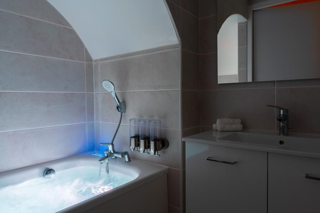 Une salle de bain moderne avec une baignoire sur pieds, une pomme de douche fixée au mur et un grand miroir au-dessus du lavabo.