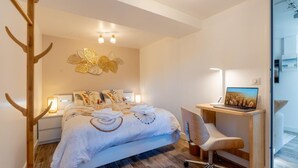 Een moderne slaapkamer met een bed, nachtlampjes, een bureau met een laptop en een decoratief wandobject.