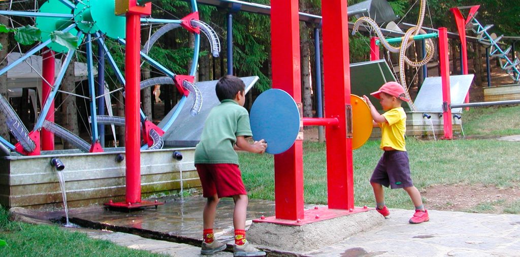 Niños jugando en un parque infantil con varios juegos, incluyendo una bomba de agua y toboganes.