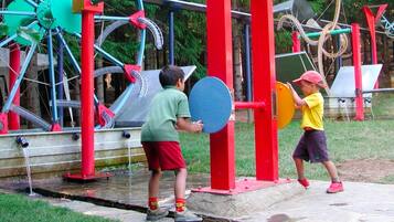 Niños jugando en un parque infantil con varios juegos, incluyendo una bomba de agua y toboganes.