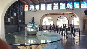 A glass-top dining table with a decorative bowl, surrounded by black chairs, in a room with arched windows and a stone wall. - Casa Rivera de Moras (Tuxcueca)