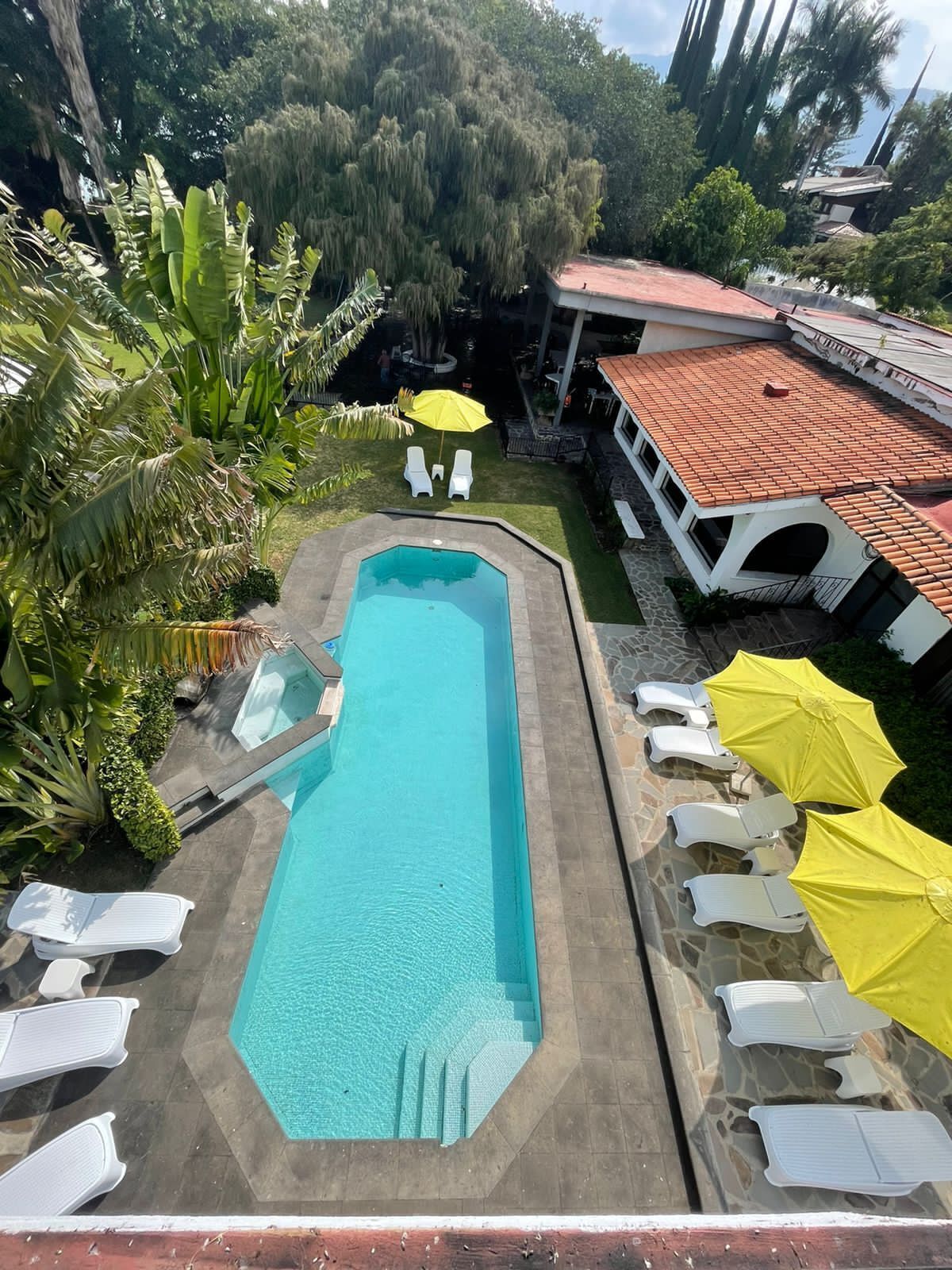 Piscina rectangular con agua azul cristalina, rodeada de sillas de descanso blancas y sombrillas amarillas.