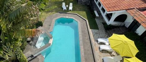 A rectangular pool with a clear blue water, surrounded by white lounge chairs and yellow umbrellas.