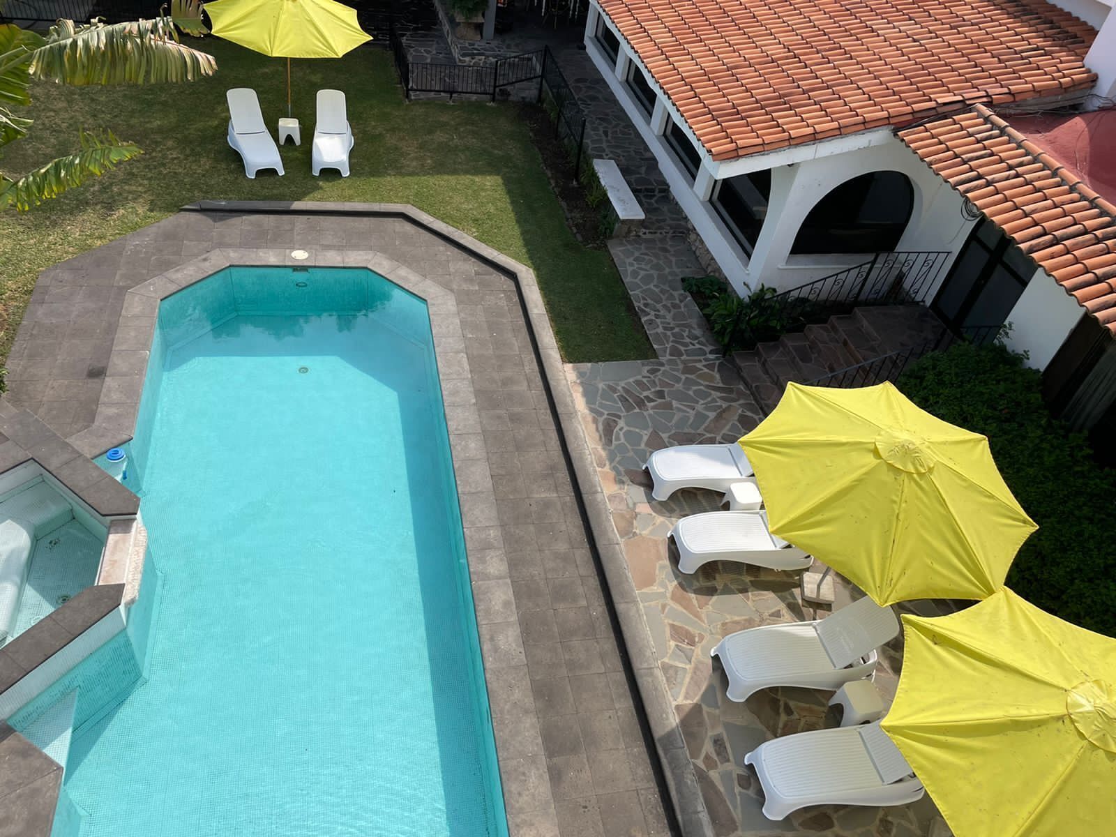 Una piscina rectangular con borde de piedra, rodeada de sillas reclinables blancas y sombrillas amarillas.