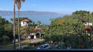 A coastal view with a restaurant sign, palm trees, and a mountain range in the background. - Casa Rivera de Moras (Tuxcueca)