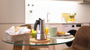 Una cocina moderna con una mesa de vidrio, una tetera, un frutero y una cafetera.