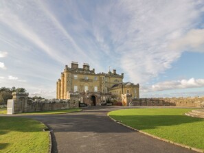 A large, historic building with a central entrance, surrounded by a well-maintained lawn and a paved driveway.