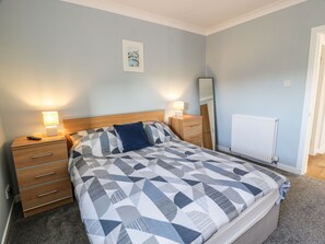 A bedroom with a bed, nightstands, a dresser, a mirror, and a radiator.