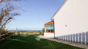 A modern building with a large window, a grassy yard, and a view of the sea.