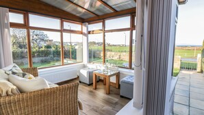 A sunroom with large windows, wicker furniture, and a view of the countryside.