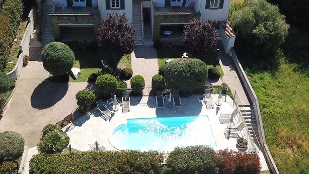 Una casa de dos plantas con piscina, rodeada de jardines y árboles bien cuidados.