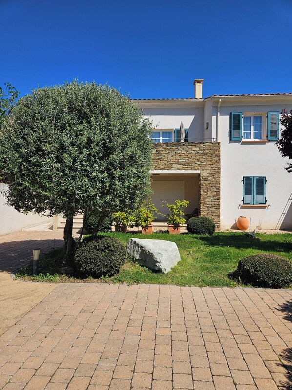 A house with a stone facade, a large tree in the front yard, and a paved driveway.