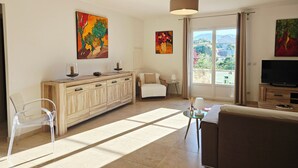 Una sala de estar con un sofá, un televisor, un mueble de madera, una silla y obras de arte en las paredes.