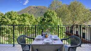 Mesa preparada para comer con vista a la montaña, sillas exteriores y una barandilla.