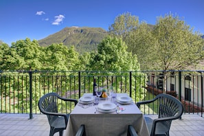 A table set for dining with a mountain view, outdoor chairs, and a railing. - Village Apartments - Porto Letizia (Porlezza)