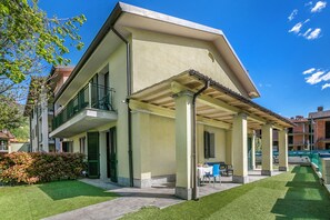 Um edifício de dois andares com um alpendre, um pequeno jardim e uma mesa com cadeiras.