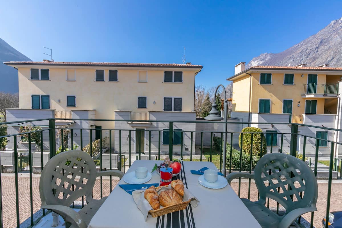 Eine Terrasse mit Frühstückstisch, einschließlich Croissants und einer roten Tasse, mit Blick auf eine Häuserreihe mit Balkonen.