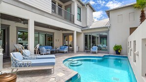 Une maison à deux étages avec une piscine, un espace salon extérieur et un balcon.