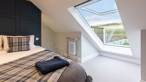 Un dormitorio con tragaluz, una cama con ropa de cama escocesa y vistas a un paisaje verde.