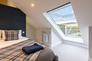 A bedroom with a skylight, a bed with plaid bedding, and a view of a green landscape.