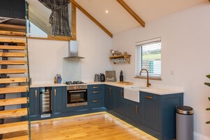 A modern kitchen with wooden flooring, built-in appliances, and a window with blinds.