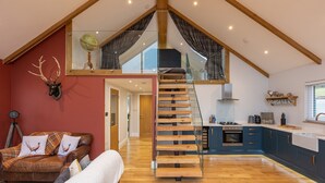 Amplio dormitorio tipo loft con escalera de vidrio, un rincón de descanso acogedor con sofá de cuero y una cocina moderna con armarios azules.
