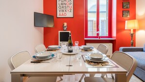 Uma sala de jantar com uma mesa posta para quatro pessoas, uma garrafa de vinho e um cartaz do alfabeto emoldurado na parede.