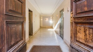 Um corredor com portas de madeira e chão ladrilhado, que leva a um quarto com uma moldura na parede.