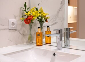 A bathroom with a white sink, two bottles of hand wash, and a vase with flowers.