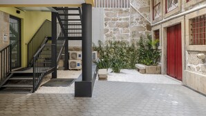 Un espace extérieur abrité, doté d’un escalier, de murs en pierre et d’une porte rouge.