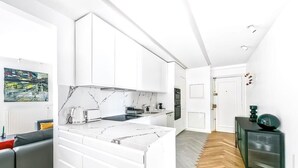 Une cuisine moderne avec des meubles blancs, un plan de travail en marbre et un parquet en bois disposé en chevrons.