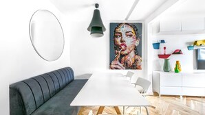 Un espace repas moderne avec une table blanche, un canapé gris et un tableau représentant une femme.