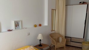 A room with two yellow beds, a wicker chair, a small table with a lamp, and a wardrobe. - ARRUBIU - small but comfy, perfect for singles, couples w. small children (P3399 (Cabras)