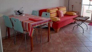 A dining area with a table set for two, a red sofa, and a floor lamp. - ARRUBIU - small but comfy, perfect for singles, couples w. small children (P3399 (Cabras)