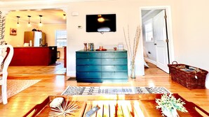 Una sala de estar con suelo de madera, un mueble azul, un televisor y una cesta.