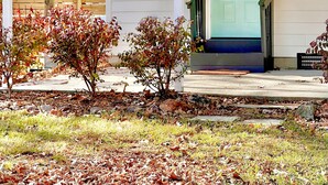 Una casa con puerta verde, un porche y un pequeño jardín con hojas cubriendo el suelo.