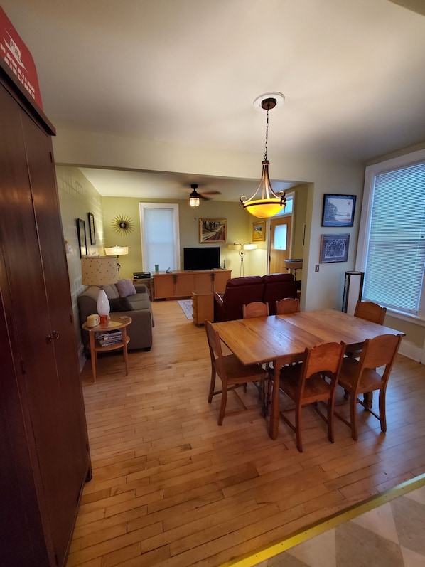 A spacious living area with a dining table, wooden floor, and a ceiling fan.