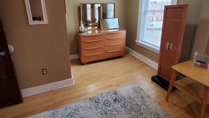 Een kamer met een houten dressoir, een spiegel, een klein tafeltje en een raam met jaloezieën.