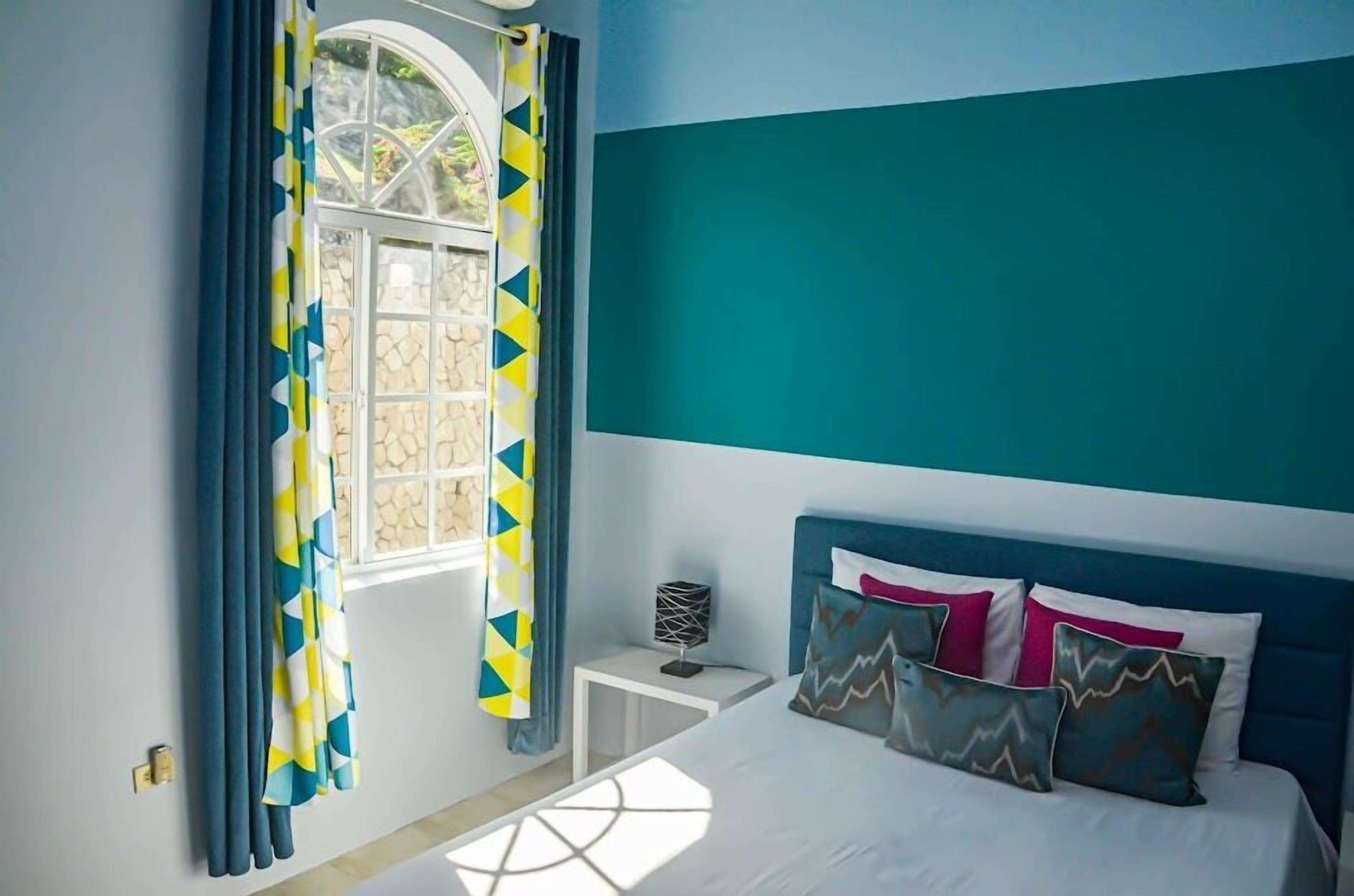 Un dormitorio con cama, mesita de noche y ventana con cortinas.