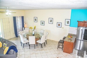 A dining area with a glass table and chairs, a kitchen with a refrigerator, and a ceiling fan. - The Shallhome  (Montego Bay)