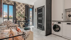 A modern apartment with a dining area, a living room with a sofa and a coffee table, a kitchen with a washing machine, and a large window with a view of buildings. - Dreams of Marbella (Marbella)