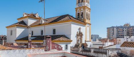 A white building with a bell tower and a clock, surrounded by a red-tiled roof and a clear blue sky.