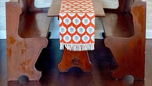 Une table en bois recouverte d’une nappe à motifs, deux chaises en bois et un mur orné d’une fresque sur le thème de la mer.