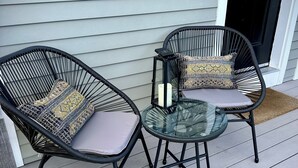 Deux fauteuils en osier avec des coussins et une table en verre, le tout placé sur une terrasse en bois.