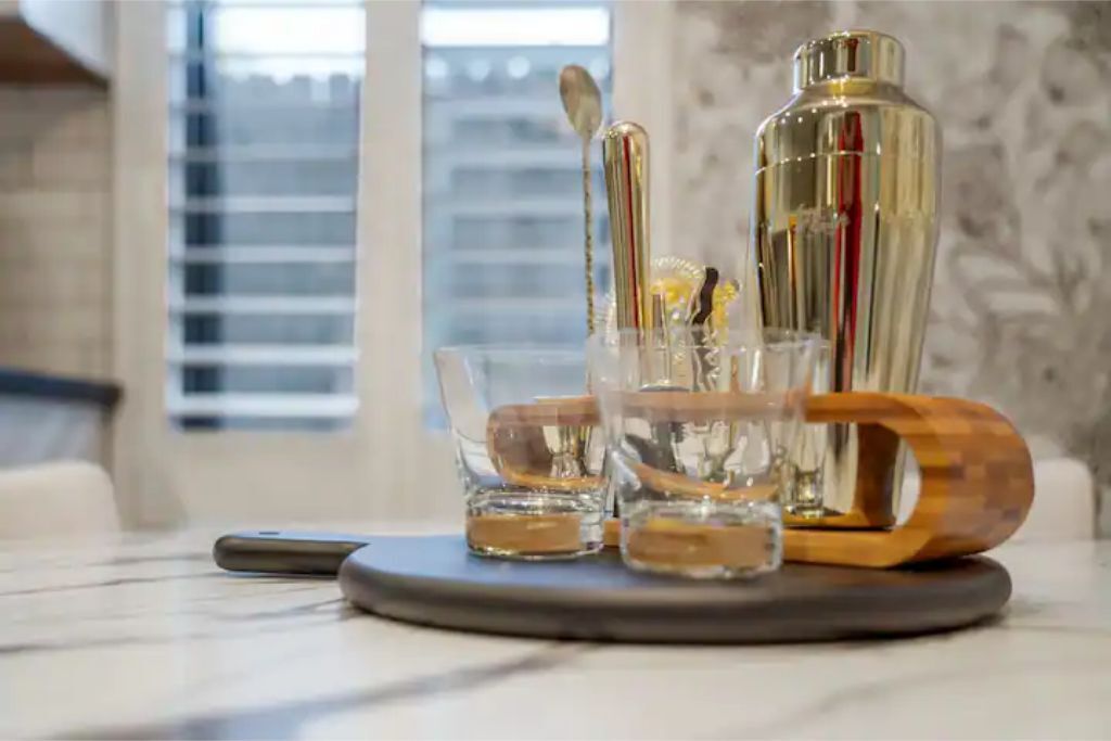 A bar area with a cocktail shaker, glasses, and a spoon on a marble countertop.