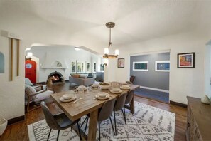 A dining area with a wooden table set for four, surrounded by chairs. A fireplace is visible in the background, and the room has a neutral color palette with gray walls and a patterned rug. - NEW listing: Modern Tudor, centrally located (Tulsa)