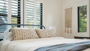 Ein Schlafzimmer mit einem Bett, einem Fenster mit Jalousien und einer Wanddekoration.